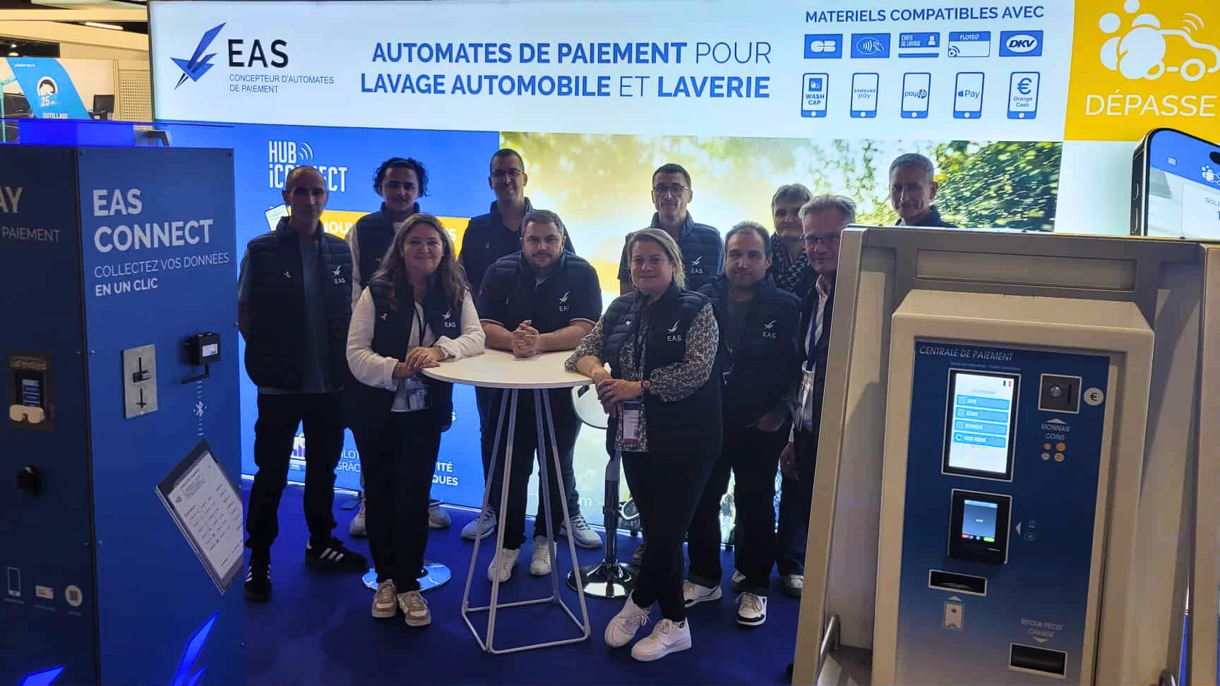 Un groupe de personnes pose devant un stand d'EAS, spécialisé dans les automates de paiement pour laveries automatiques et 